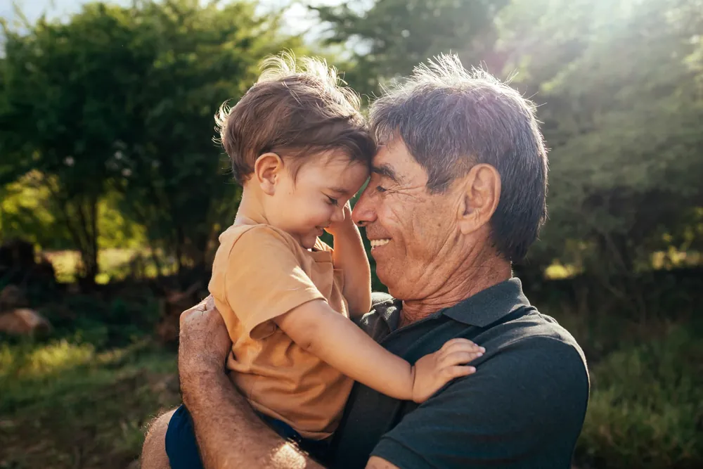 An older man holding a young child outdoors, foreheads touching