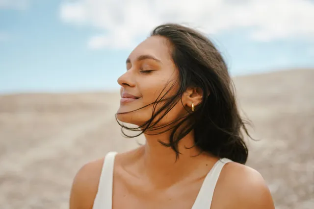 A smiling woman outdoors with her eyes closed and the wind in her hair